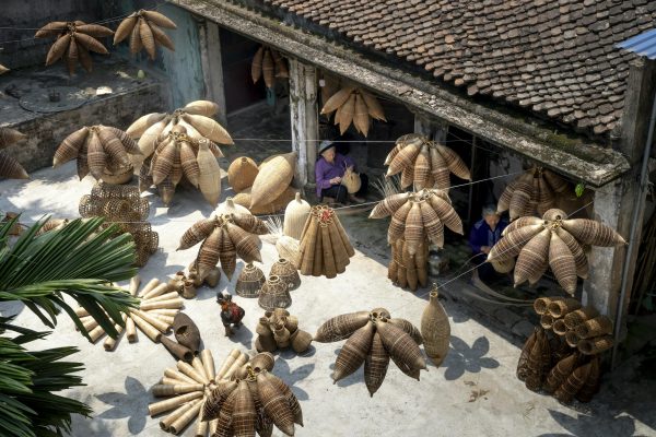 From above of people sitting and making bamboo fish traps while working on local bazaar in Vietnam in daylight